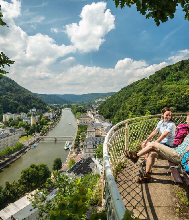 Zwei Frauen die auf einer Bank auf einem Aussichtspunkt sitzen und auf eine Stadt am Fluss schauen.