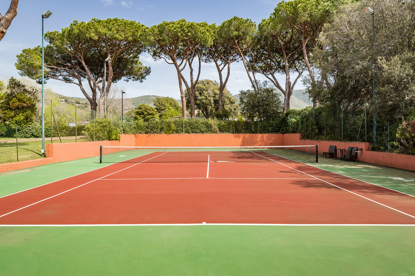 Tennisplatz mit rot-grünem Boden umzingelt von Bäumen
